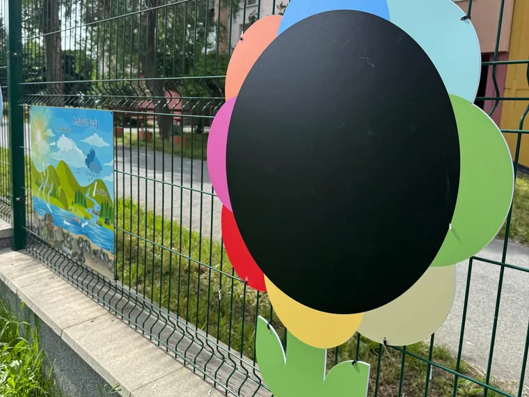 Kresliaca tabuľa v tvare kvetu na plote materskej školy, vedľa nej edukačná tabuľa